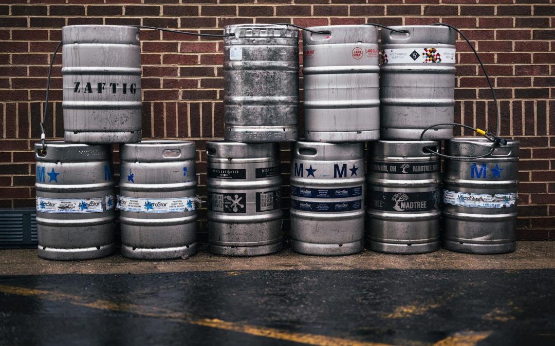 Row of metallic beer kegs stacked outside a brick wall, showcasing brewing industry.